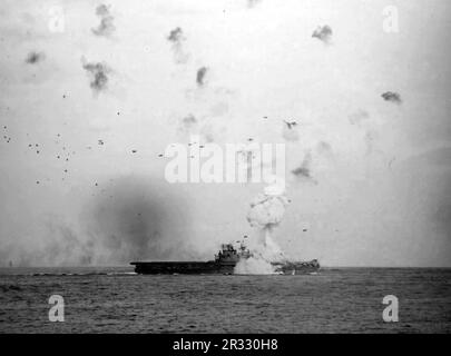 The U.S. Navy aircraft carrier USS Enterprise (CV-6) at the moment being hit by a Japanese bomb-laden kamikaze on 14 May 1945. The ship's forward elevator was blown approximately 400 feet into the air from the force of the explosion six decks below. When Japan was facing defeat in late 1944 it chose to destroy US ships with suicide bombings, known as Kamikaze.These attacks were a potent physical and psychological weapon and sunk a total of 47 ships at a cost of more than 3000 pilots and planes. By late 1944 the US Navy was large enough that the losses were insignificant and they did not alter Stock Photo