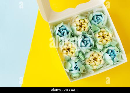 Yellow-blue marshmallow in the form of flowers in the form of tulips. Marshmallow in a box on a yellow-blue background. View from above Stock Photo