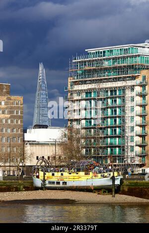 Tamesis Dock pub in converted 1930’s Dutch barge at low tide, apartment buildings on the Albert Embankment, The Shard Tower in background, London, UK Stock Photo