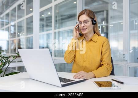 Portrait of a young woman in a headset working in an office center online from a laptop. Stock Photo