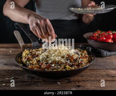 Woman sprinkles cheese over a pan with farmers breakfast. Stock Photo