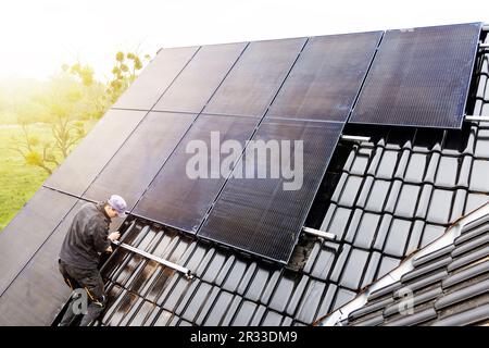 Technician installing solar panels on the roof of a house Stock Photo