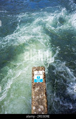 Water rushing past a concrete pier with a danger keep off sign Stock Photo