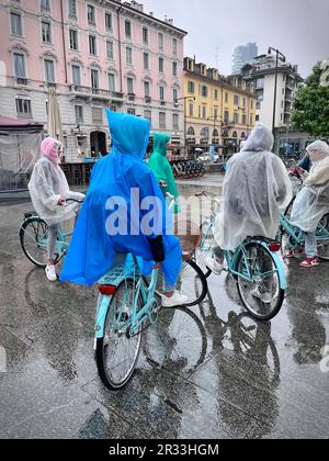 Group of cyclists on a rainy day in the city wearing rain coats. Milan, Italy - May 2023 Stock Photo