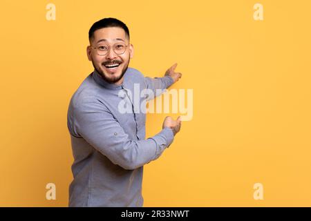 Cheerful Excited Asian Man Pointing At Copy Space On Yellow Background Stock Photo
