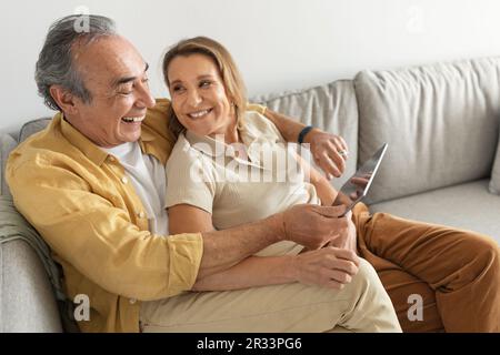 Happy senior married couple enjoying digital gadget world using tablet computer, websurfing or watching film online Stock Photo