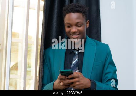 young african business man wearing a suit smiling and using his mobile phone in the office Stock Photo