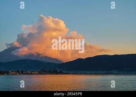 Sunset in the mountains on the coast of the Aegean Sea, the clouds above the mountain are illuminated by the setting sun, in the background there is a Stock Photo