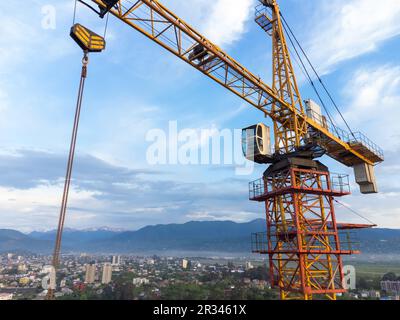 Close-up view from a drone of a construction crane cabin against the backdrop of beautiful mountains and sky. Construction concept Stock Photo