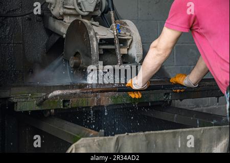 A worker cuts granite. The cutter cuts granite. Stone processing machine. Stone cutting at the factory Stock Photo