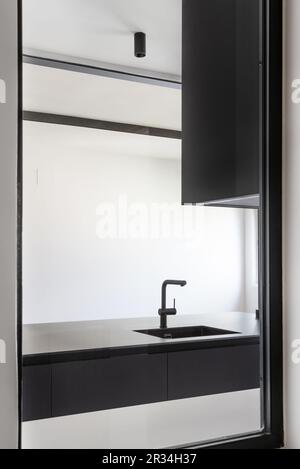 A skylight in a kitchen furnished with smooth black cabinets without handles, a black sink with a matching faucet, and black track lighting Stock Photo