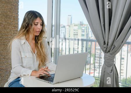 young latin freelance woman concentrated working at home with her laptop, sitting in the living room with her laptop, business concept, copy space. Stock Photo