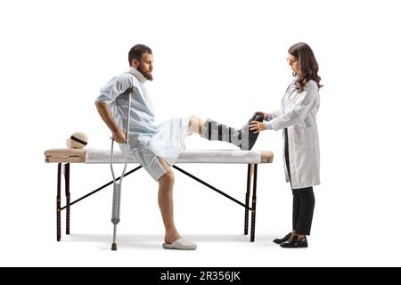 Female doctor putting on a walking brace to a male patient in a hospital gown isolated on white background Stock Photo