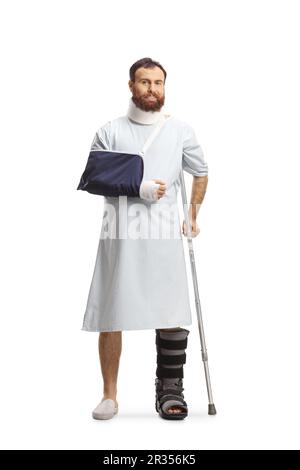 Bearded man in a hospital gown with a broken leg and arm and neck collar isolated on white background Stock Photo