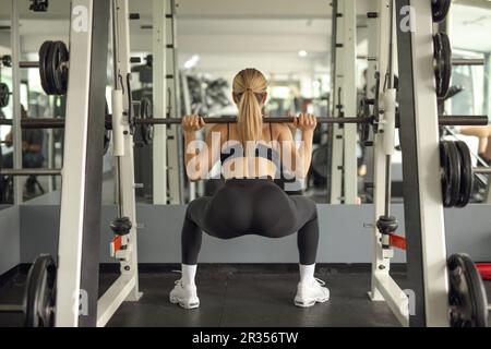 Rear view shot of a fit woman lifting a weight bar in a gym in front of a mirror Stock Photo