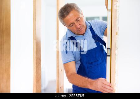 Man builder in blue overalls measures deviations from a given vertical wall using building level Stock Photo