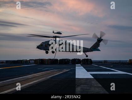 230517-N-MZ309-1132 ATLANTIC OCEAN (May 17, 2023) An MH-60S Knighthawk helicopter, attached to Helicopter Sea Combat Squadron (HSC) 5, moves ordnance aboard the Nimitz-class aircraft carrier USS George H.W. Bush (CVN 77) during an ordnance transfer with the Supply-class fast combat support ship USNS Supply (T-AOE 6), May 17, 2023. George H.W. Bush provides the national command authority flexible, tailorable war fighting capability through the carrier strike group that maintains maritime stability and security in order to ensure access, deter aggression and defend U.S., allied and partner inter Stock Photo