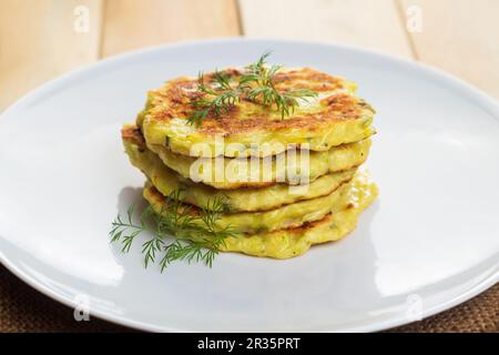 Stack of zucchini pancakes on white plate. Healthy vegan diet food close-up. Green vegetarian fritters. Stock Photo