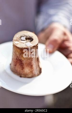 A person holding a roasted marrow bone on a plate (street food) Stock Photo