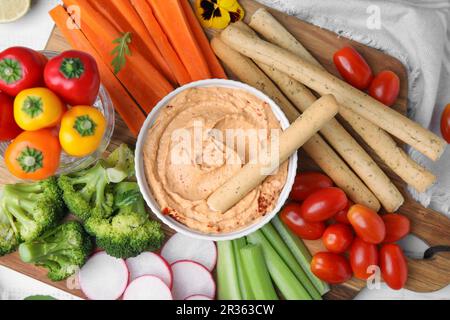 Board with delicious hummus, grissini sticks and fresh vegetables on white background, flat lay Stock Photo