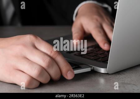 Man connecting usb flash drive to laptop at grey table, closeup Stock Photo