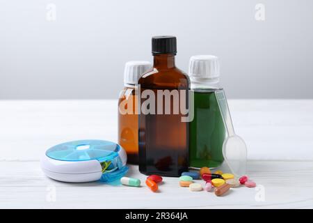 Bottles of syrup, dosing spoon and pills on white table against light grey background. Cold medicine Stock Photo