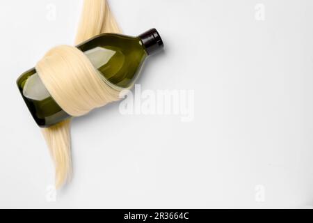 Shampoo bottle wrapped in lock of hair on white background, top view. Space for text Stock Photo
