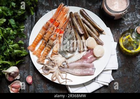 Various types of seafood on a plate with olive oil, herbs and garlic Stock Photo