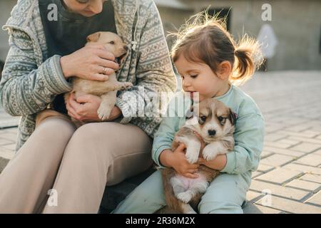 Happy family of mother and daughter relaxing and sharing moment of love petting the puppies outdoors, trust and care. Mother nature. Cute animal. Stock Photo