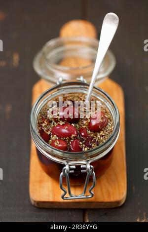 Pickled kalamata olives with oregano in glass jar on a chopping board Stock Photo