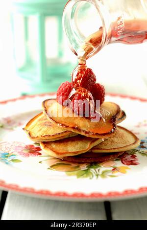 Maple syrup being poured over pancakes with raspberries Stock Photo