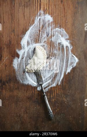 Maultasche (German pasta dish) on an old wooden board with flour and a fork Stock Photo