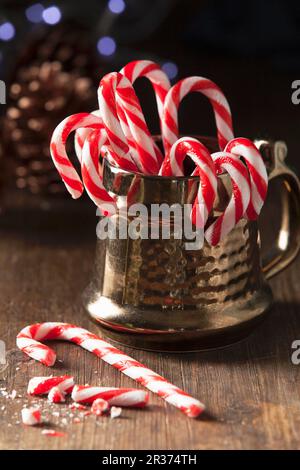 Christmas candy cane in a traditional style gold mug with one whole can on the table with broken candy can pieces Stock Photo