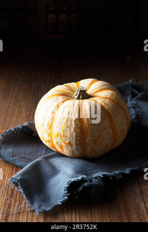 A munchkin pumpkin on a frayed, dark blue linen napkin Stock Photo