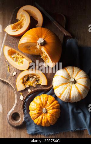 A piece of pumpkin on a wooden chopping board and munchkin pumpkins on a blue linen napkin Stock Photo