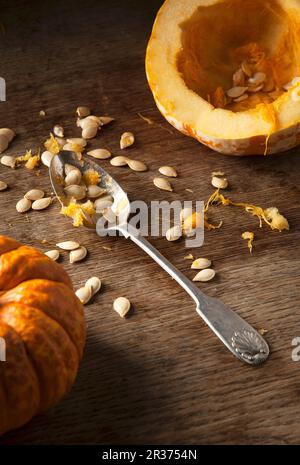 A hollowed out munchkin pumpkin, pumpkin seeds and a vintage spoon on a rustic wooden background Stock Photo