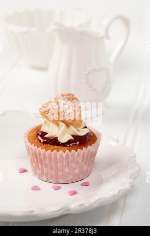 A sweet heart cupcake on a white plate with white milk jug and sugar basin in background Stock Photo