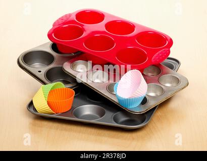 A selection of different types of baking trays and cases for making cupcakes shown on a wooden surface Stock Photo