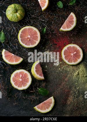 Sliced pink tiger lemon with mint leaves on branches with pink and green powder Stock Photo