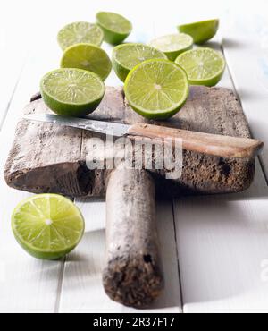 Halved limes on an old wooden board with a knife Stock Photo