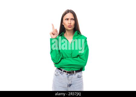 portrait of a smart pensive slim cute brown-eyed brunette woman dressed in a green shirt smiling on a white background with copy space Stock Photo