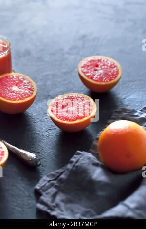 Blood oranges, whole and halved, on a grey concrete surface Stock Photo