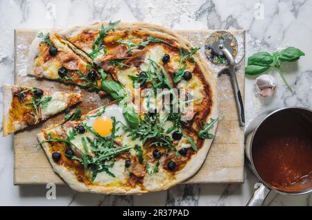 Pizza with tomato sauce, fried egg, rocket, olives and parmesan (top view) Stock Photo