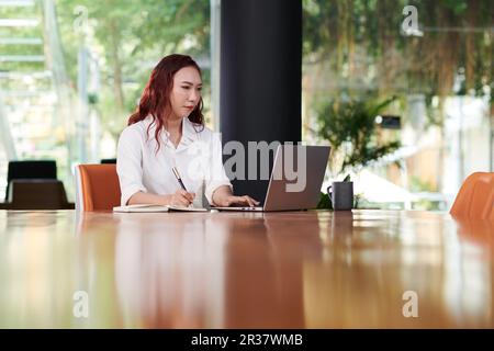 Serious businesswoman watching presentation on laptop and taking notes in planner Stock Photo