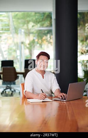 Portrait of smiling entrepreneur working on laptop at office desk in meeting room Stock Photo