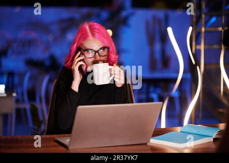 Businesswoman answering late phone call from another country and drinking coffee Stock Photo