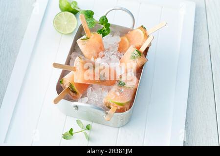 Lime and papaya ice lollies with mint on crushed ice in a metal tray Stock Photo