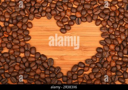Heart shaped coffee beans frame over bamboo wood background Stock Photo