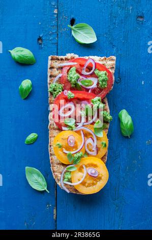 Open sandwich, grilled baguette with yellow and red tomatoes, basil pesto and red onion Stock Photo