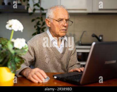 gray haired old man working at laptop at home Stock Photo